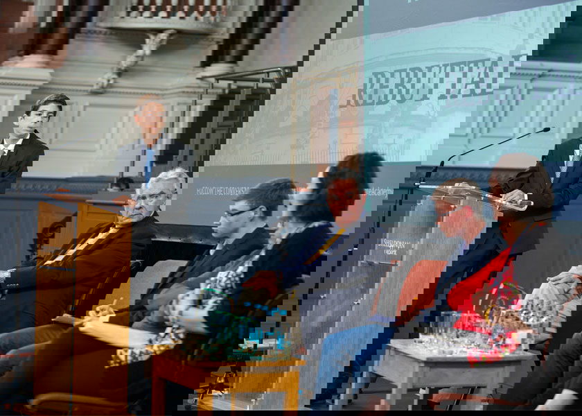 Students take part in a debate, with a professor watching. 