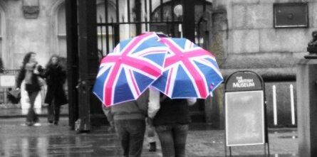 A couple of people stand in front of the British museum, hidden by huge Union Jack umbrellas.