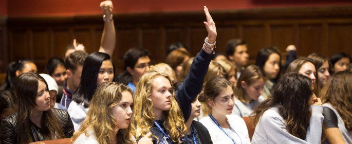 Image shows a student raising her hand in a debate.